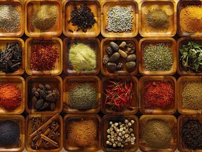 A large selection of commonly used Indian cooking spices in wooden trays on an old table. Spices include, chili ,cumin, tumeric, corriander, cumin, cardamon, garam masala, saffron, cinamon and star anise, poppy seed, sesame, cloves, nutmeg, black and white pepper corns, aniseed and fenugreek.
